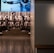 A dimly lit display features statues of athletes standing on a podium. They are positioned in front of a backdrop with the words 'LEVELING THE PLAYING FIELD' in bold letters. On the wall to the right, a softly lit quote is partially visible. The overall ambiance suggests a museum or exhibition setting.